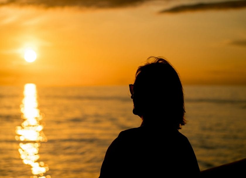 Shows a woman looking at the Sunset  on a cruise