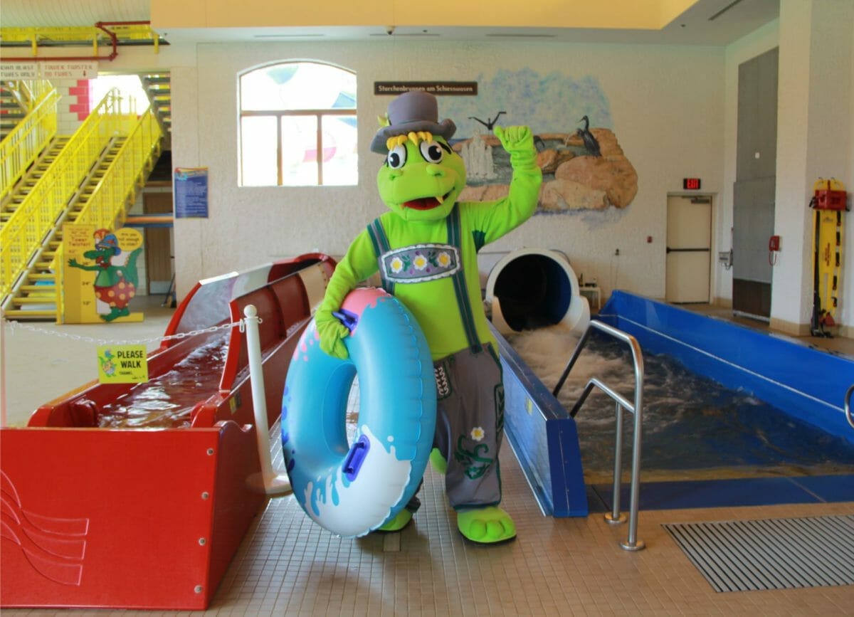 Show the mascot of the Bavarian Inn, Willy holding an inner tube at the top of a slide, indoor water parks in Michigan