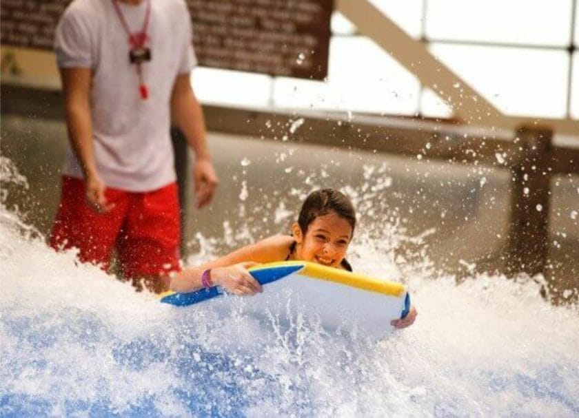 Picture of a girl riding a wave with a lifeguard standing behind her at Wild Water Dome Indoor Water Park in Gatlinburg, TN, Tennessee Indoor Water Parks