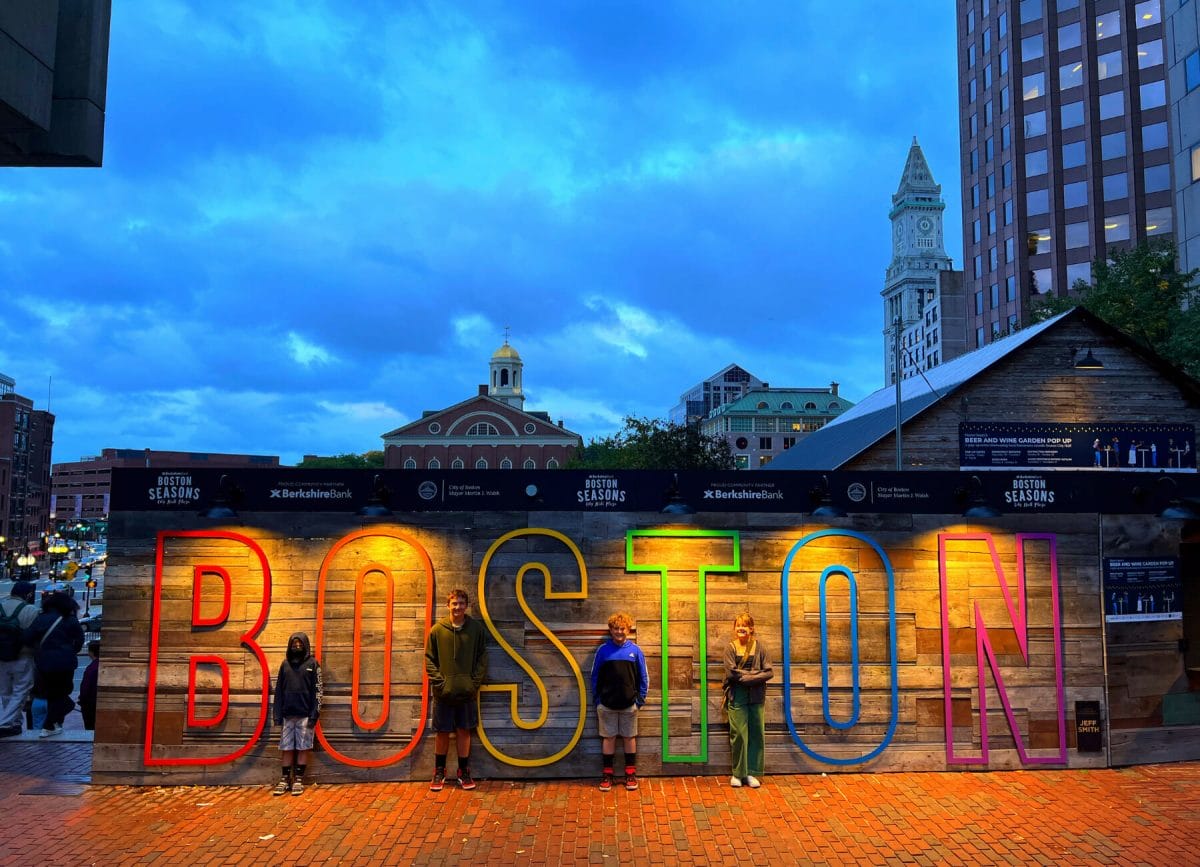 Picture of kids standing in front of the Boston sign with the twilight sky in the background, Things to do in Boston with kids.