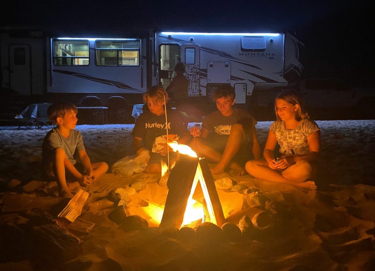 Shows children sitting around a campfire in front of an RV, Best Campfire Starter Kits