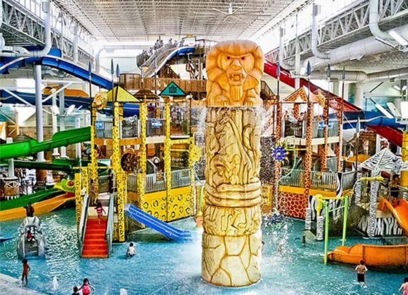Shows a large totem pole in front of a massive play structure in a pool, indoor water parks Wisconsin