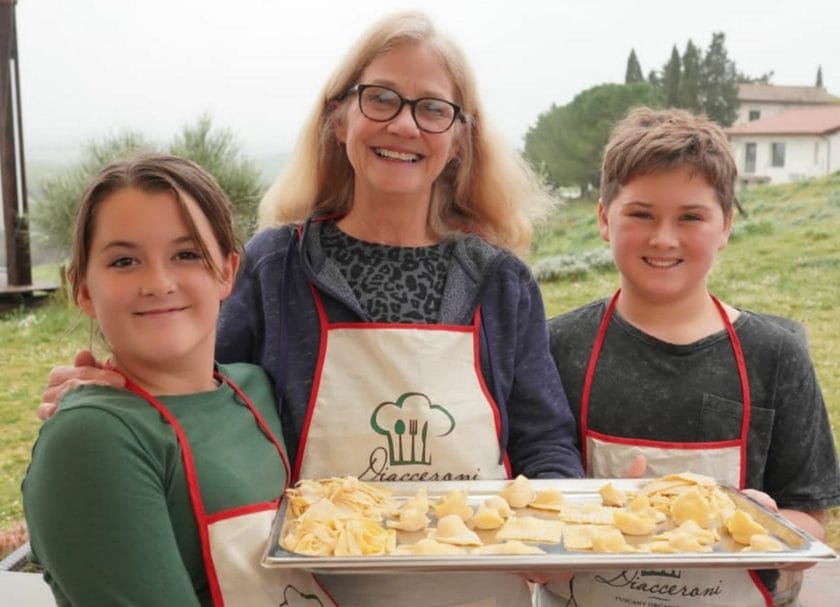 Smiling kids and an adult holding a tray of pasta they made, Things to do in Tuscany.