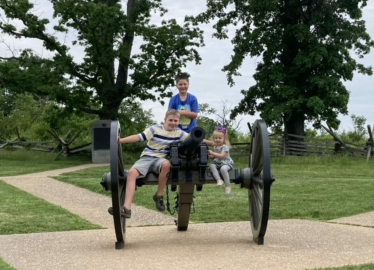 Shows 3 children sitting on top of a cannon in the battlefield, things to do in Gettysburg.