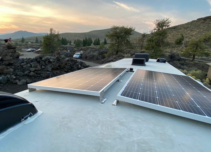 Shows a close up view of an RV roof with the solar panels, there are hills and a sunset in the background, Best RV Roof Sealants