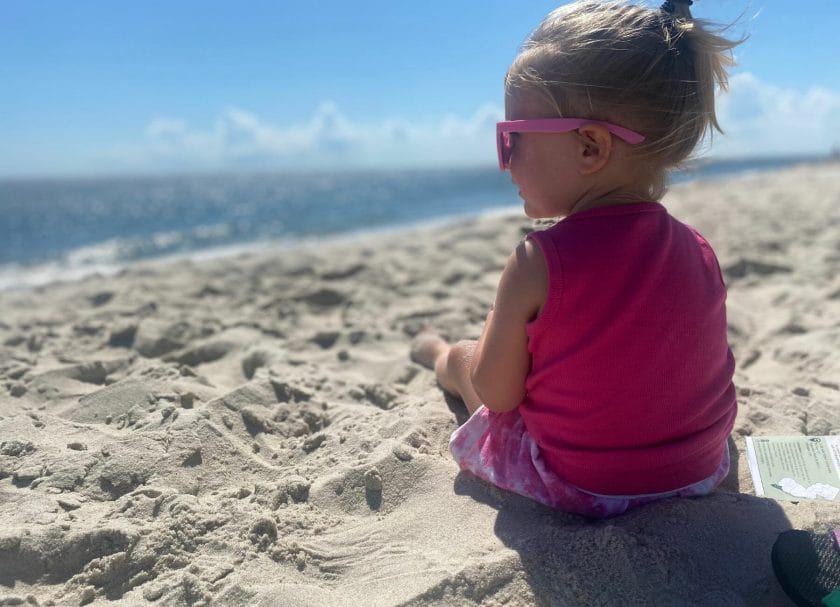 Shows a little girl in pink sunglasses sitting on the beach staring at the ocean, Things to do in Cape May, New Jersey