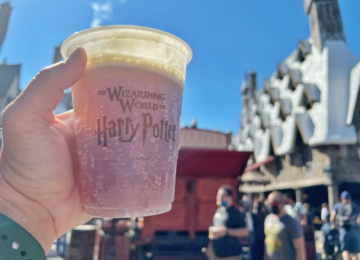 Shows a hand holding a cup of Butter Beer in the Wizarding World of Harry Potter, Harry Potter World Rides