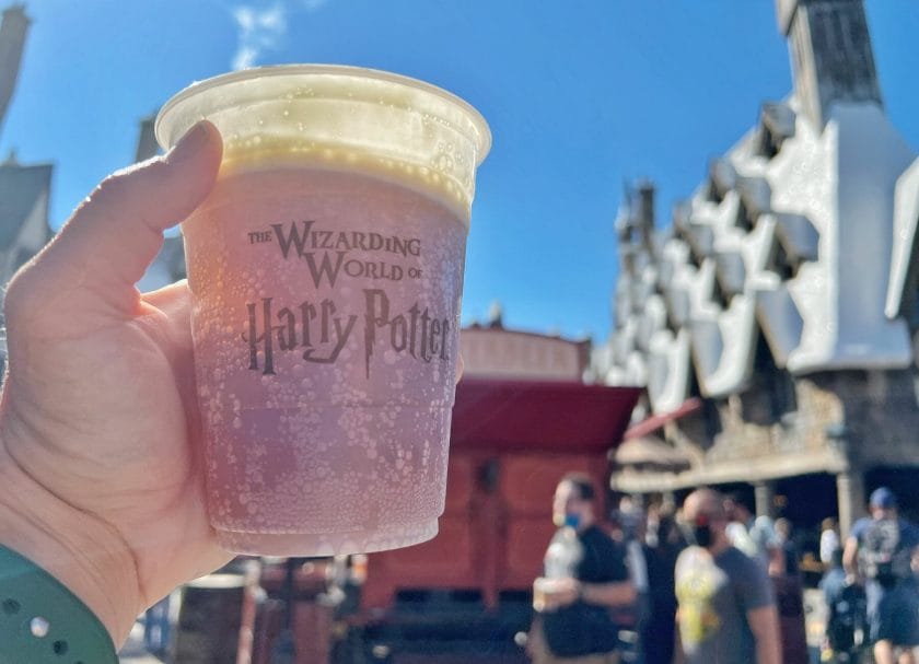 Shows a hand holding a cup of Butter Beer in the Wizarding World of Harry Potter, Harry Potter World Rides