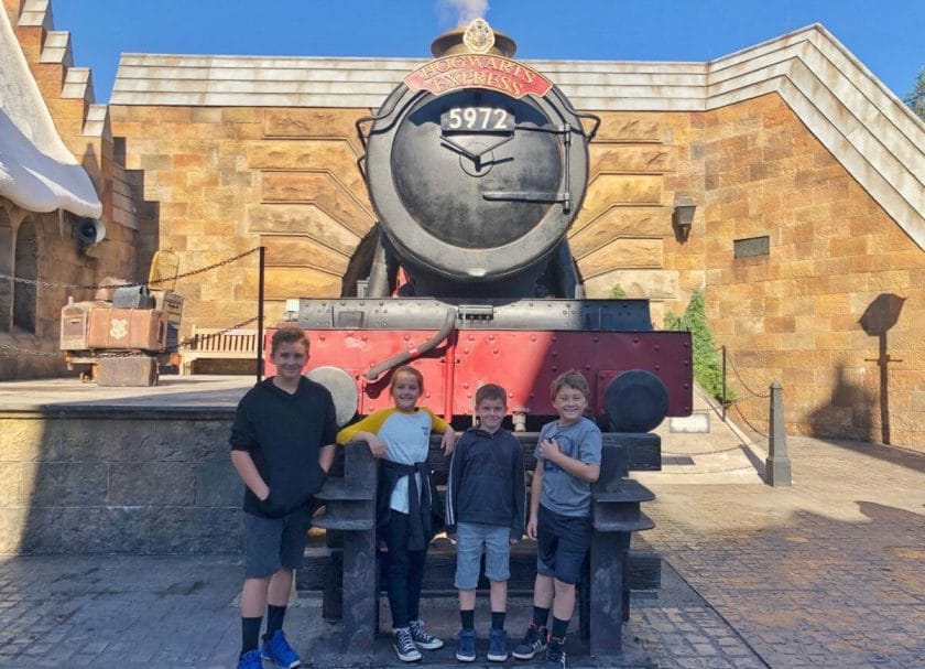 Shows 4 kids standing in front of the Hogwarts Express, Harry Potter World Rides