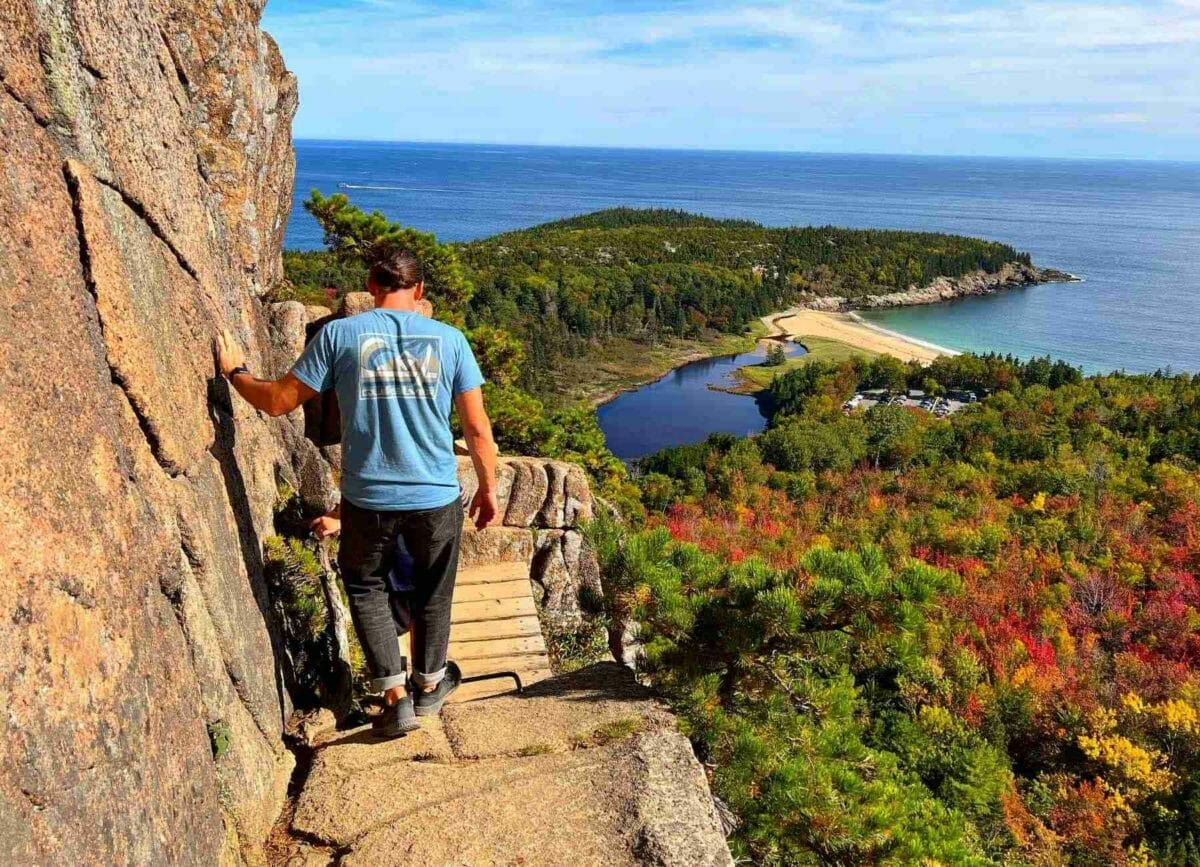 man climbing down the side of a cliff on Beehive Trail overlooking Acadia National Park