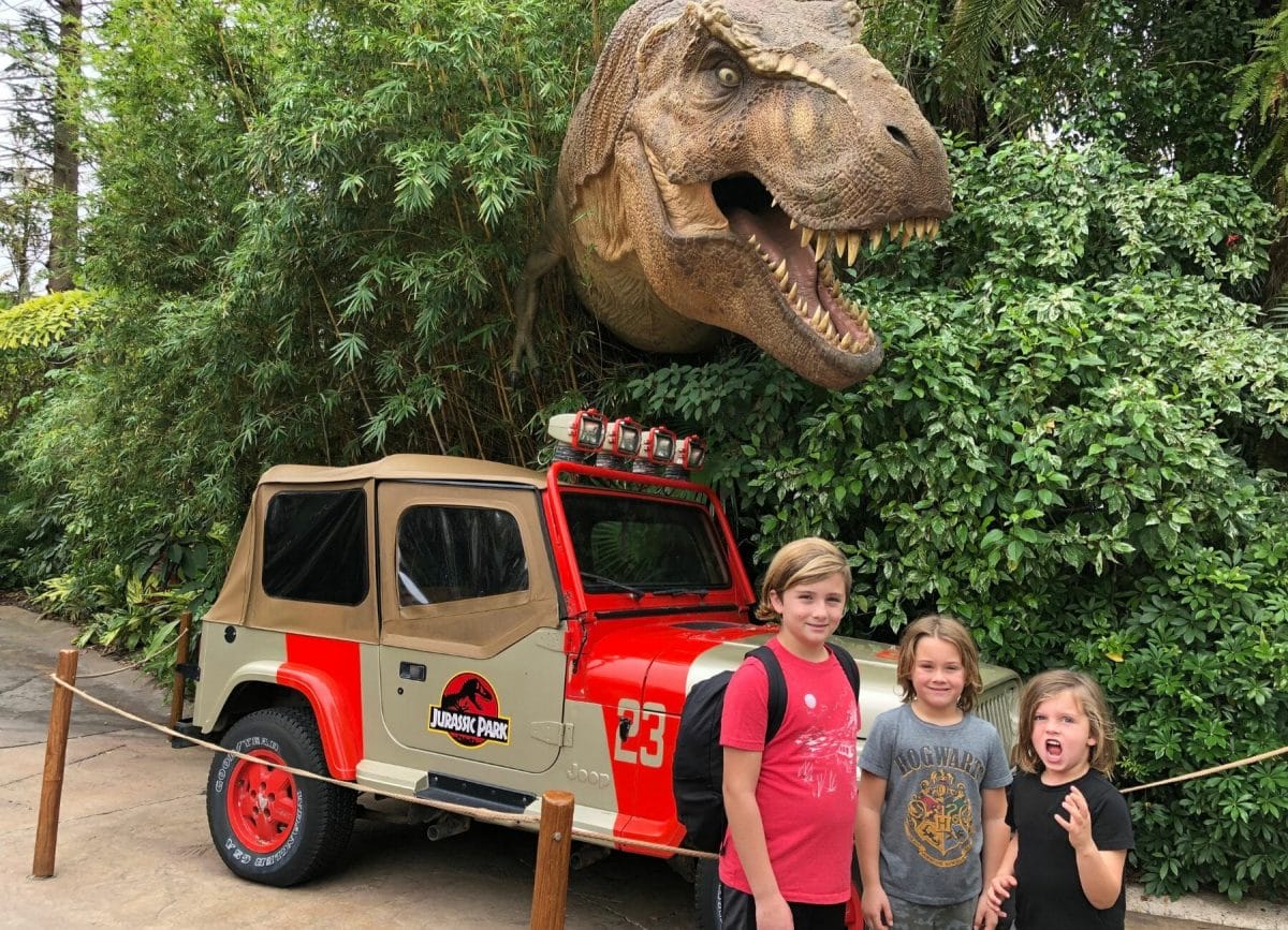 Shows 3 boys standing in front of a dinosaur at Jurassic Park, Universal Studios vs Islands of Adventure