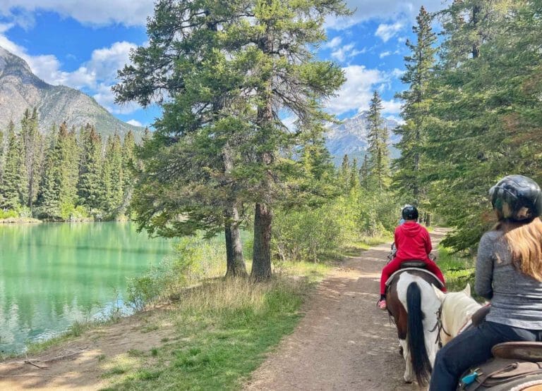 Melia and Cannon walking along the river with their horses in Banff National Park.
