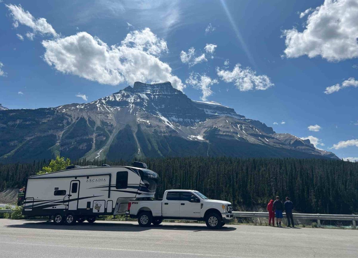 Keystone Arcadia RV in front of mountains with Dad and 2 kids. 
