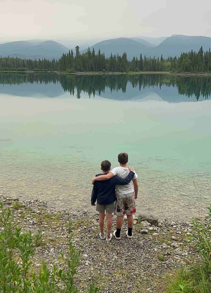 2 kids in front of a lake with a forest and mountains 